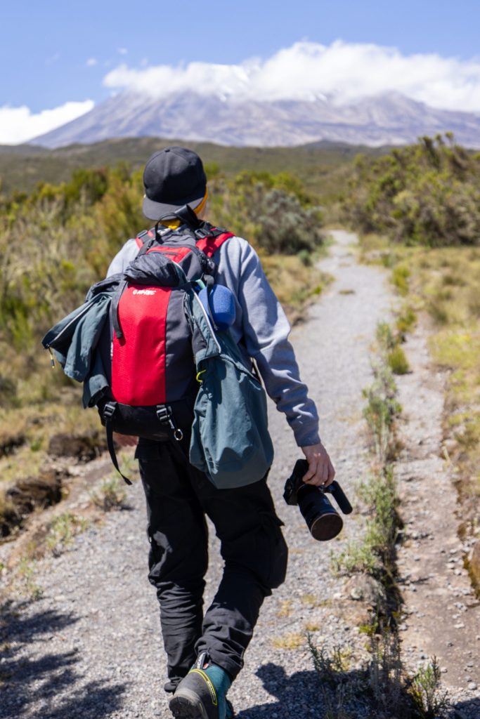 A man hiking on a trail with a camera and backpack towards Mount Kilimanjaro.